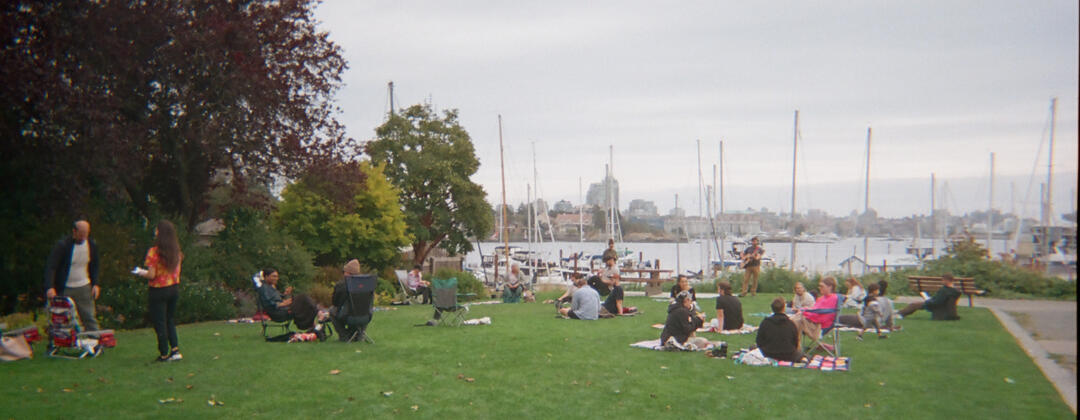 A photo of people sitting on a field overlooking a marina on the water.